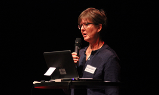 Bild på Merike Hansson som håller i en mikrofon och föreläser